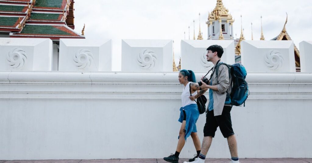 タイの寺院の塀沿いを、小さなバッグとリュックだけで歩く2人の旅行者